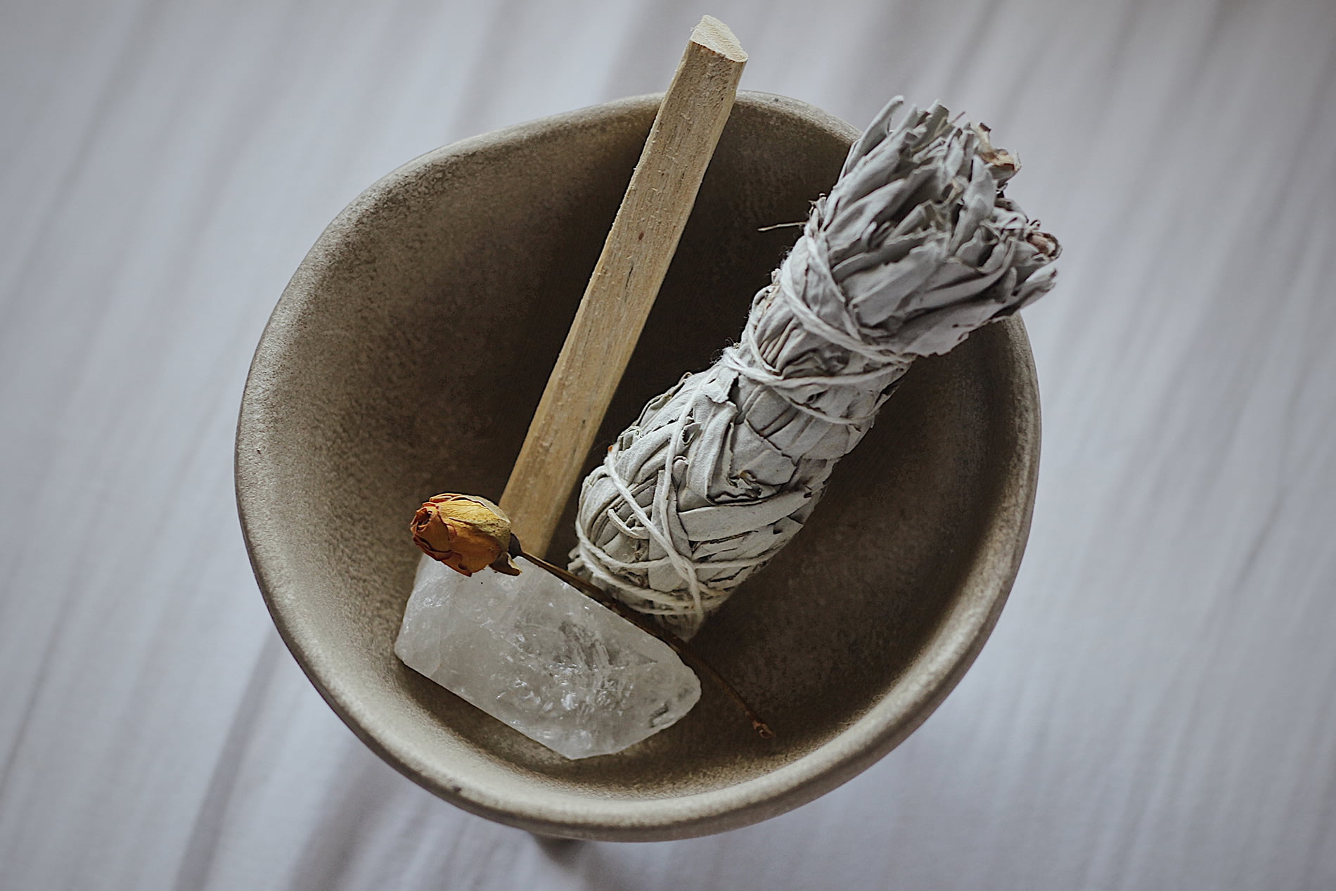 Photos des outils pour purifier sa maison: de la sauge, un quartz rose, un bâton d’encens et u  bol tibétain